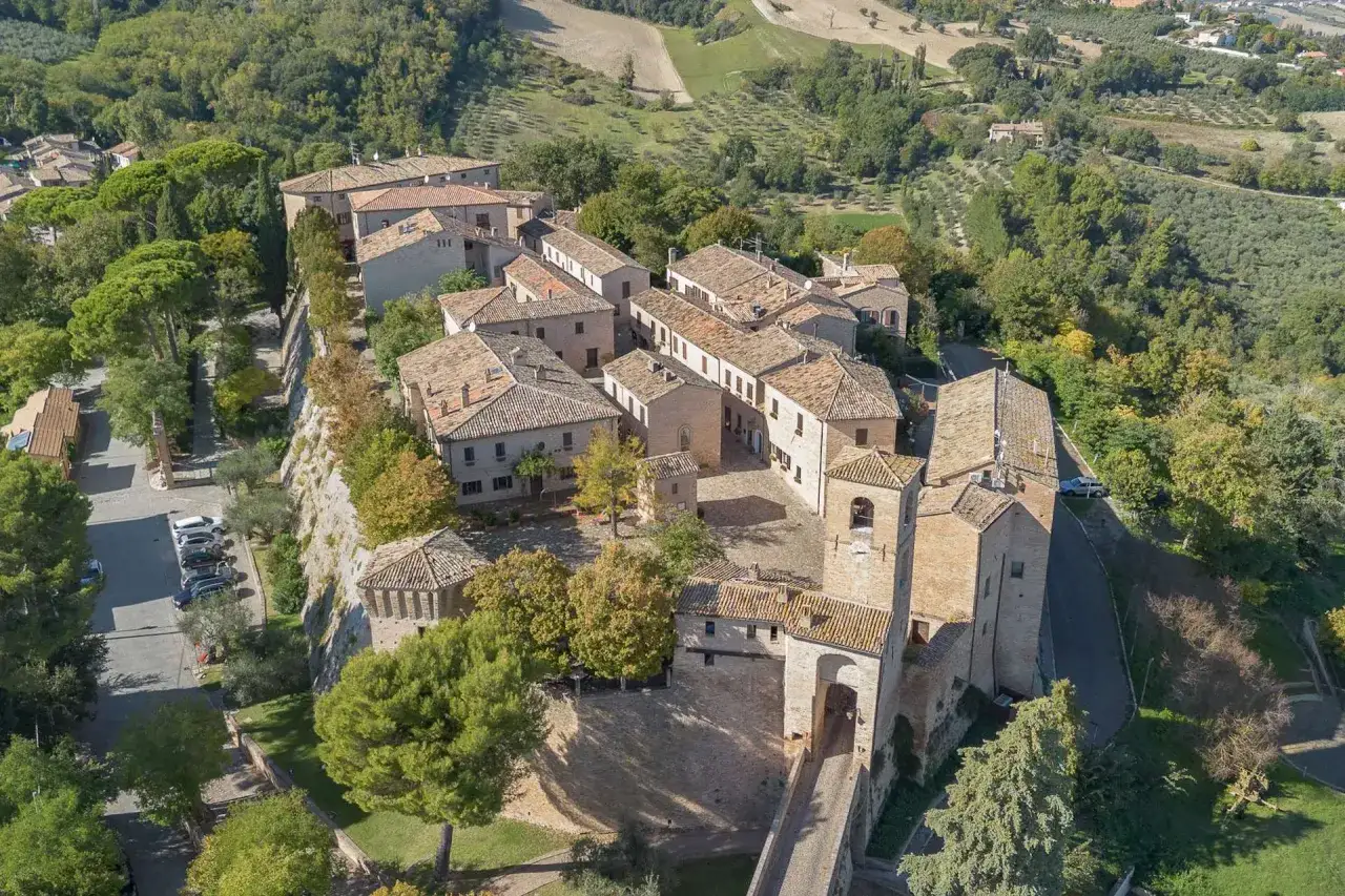 Borgo medievale di Montegridolfo cosa vedere: un castello con torre campanaria, case in pietra e tetti in cotto, immerso nel verde delle colline.
