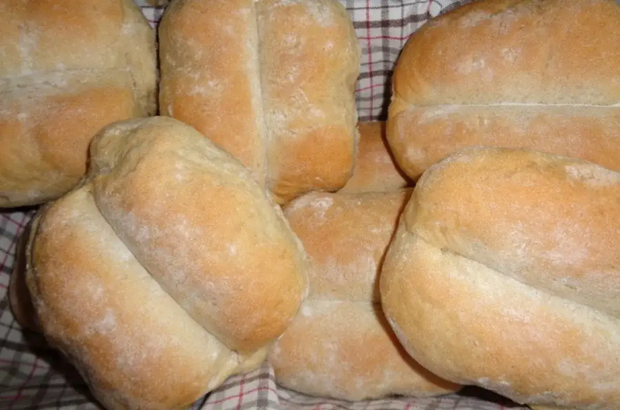 Świeżo upieczone bułki pszenno żytnie, lekko oprószone mąką, ułożone na kratkowanym materiale.