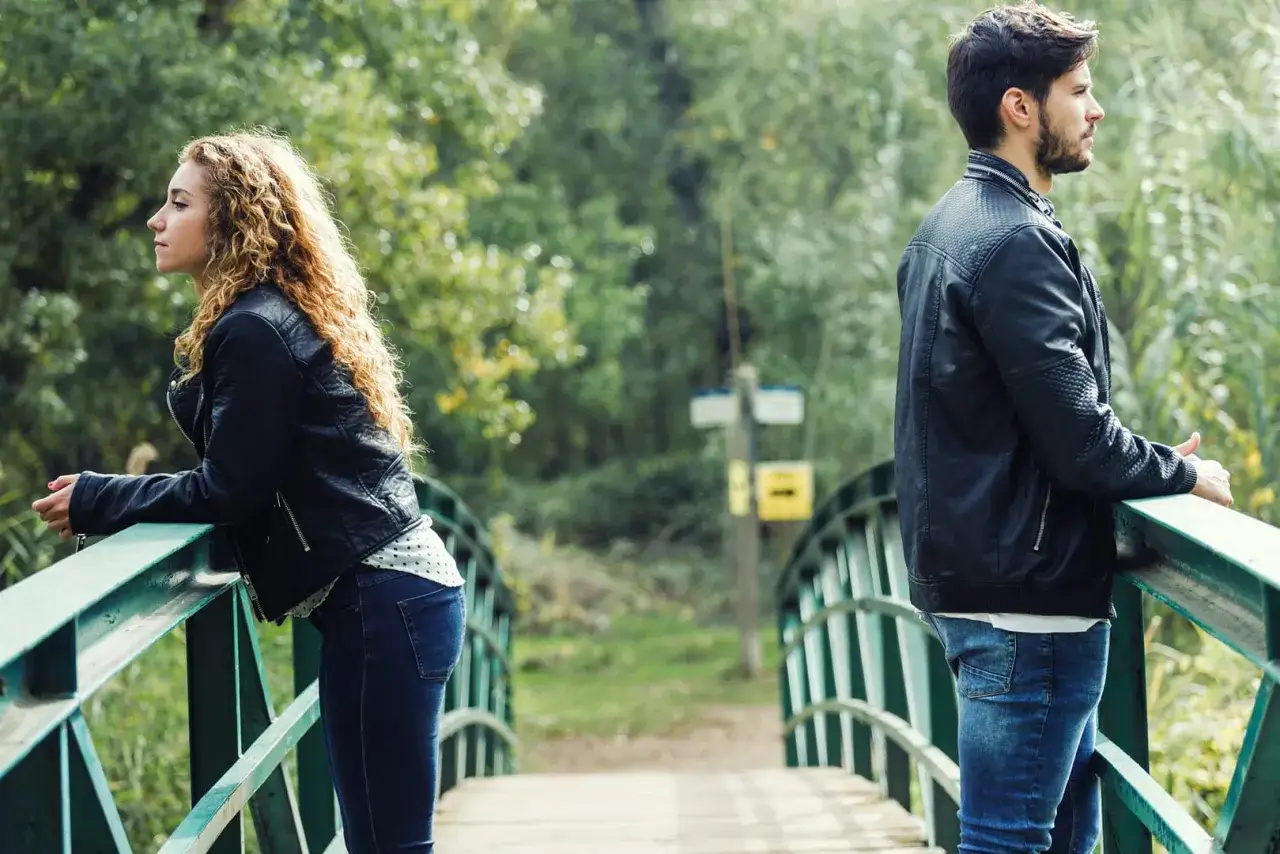 Ein Mann und eine Frau stehen auf einer Br&uuml;cke, jeder in eine andere Richtung blickend. Ein Bild, das eine einseitige Beziehung testet.