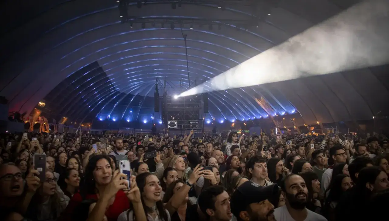 Multitud disfrutando de un concierto en el espacio Zity. Luces y humo crean una atmósfera vibrante mientras los asistentes graban el momento con sus móviles.