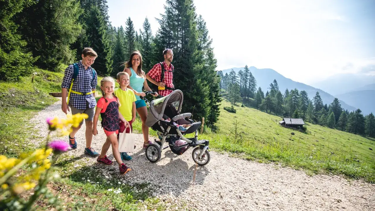Famiglia in passeggiata su sentiero montano, con passeggino per neonati, godendosi l'aria fresca e l'alta altitudine.