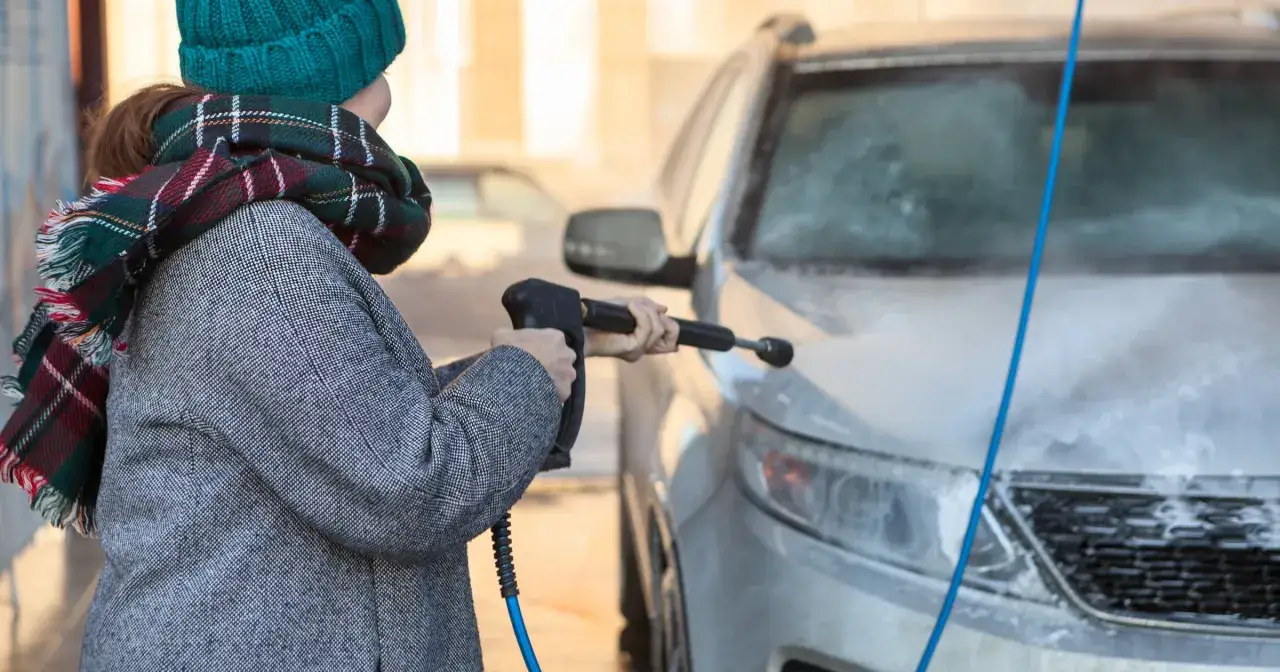 Kobieta w czapce i szaliku myje auto myjką ciśnieniową. Czy można myć auto w mrozie? To pytanie zadaje sobie wiele osób, ale ta pani chyba wie, że można!