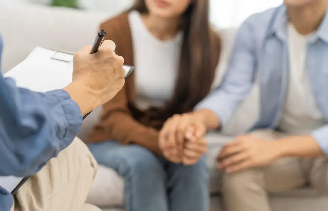 Coppia in terapia, lei tiene la mano del suo ragazzo che &egrave; depresso, mentre il terapeuta prende appunti.