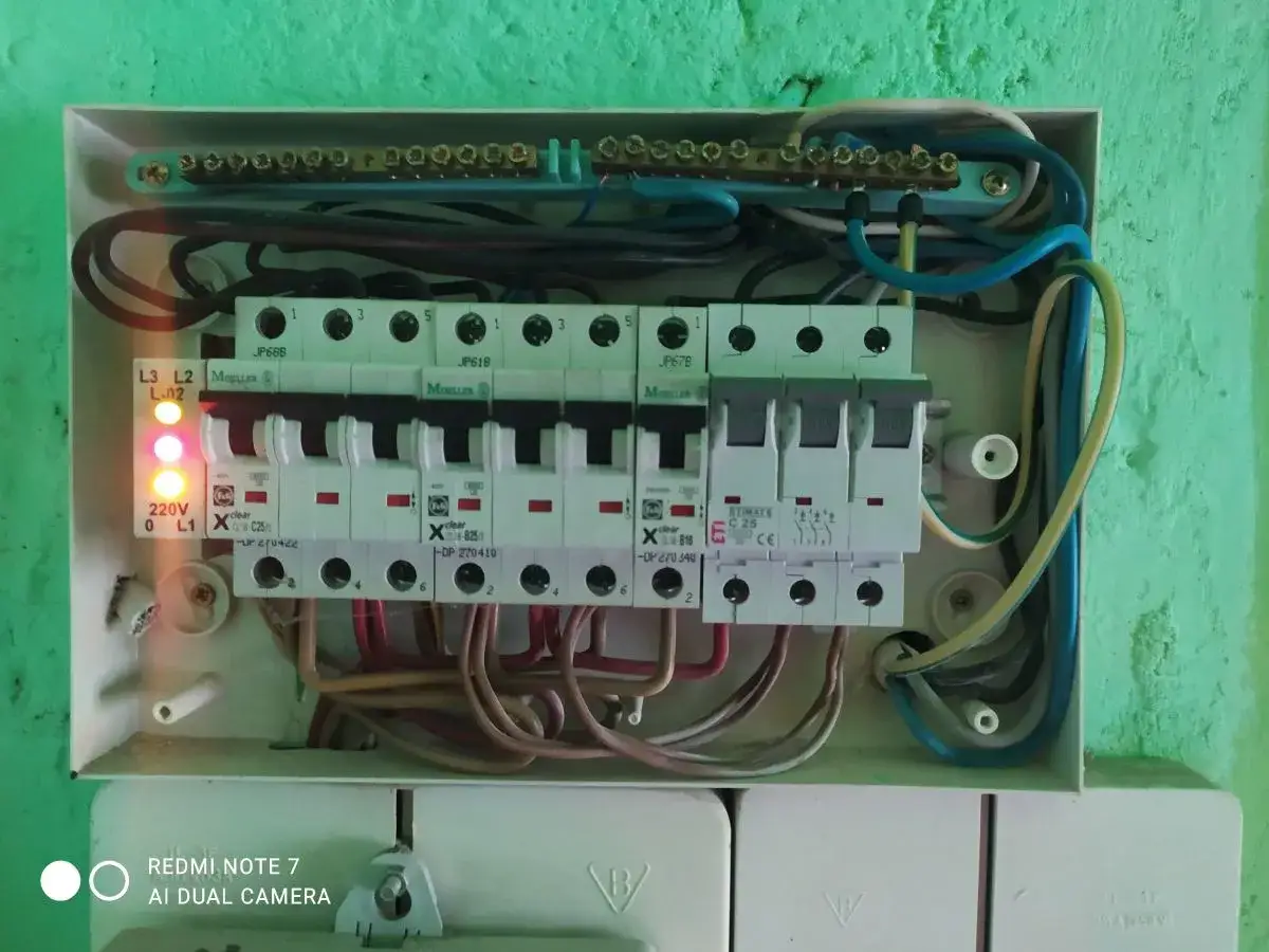 W skrzynce elektrycznej widać bezpieczniki i przewody. Dwa czerwone wskaźniki sygnalizują problem, być może spadek napięcia.