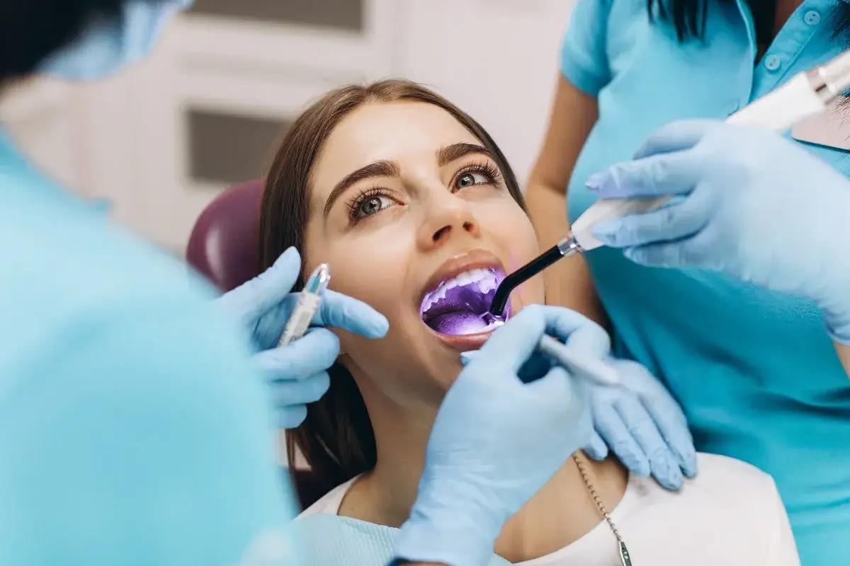 Dentysta utwardza światłem lampy **plombę tymczasową** w zębie pacjentki.