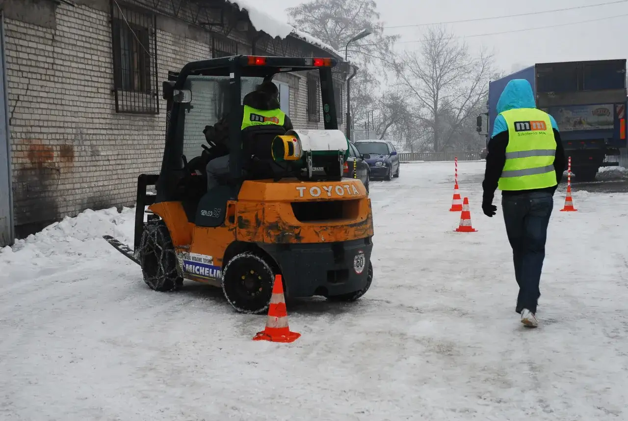Zima w Krakowie. Kurs na wózek widłowy w trudnych warunkach. Kierowca w kamizelce odblaskowej, teren zasypany śniegiem.