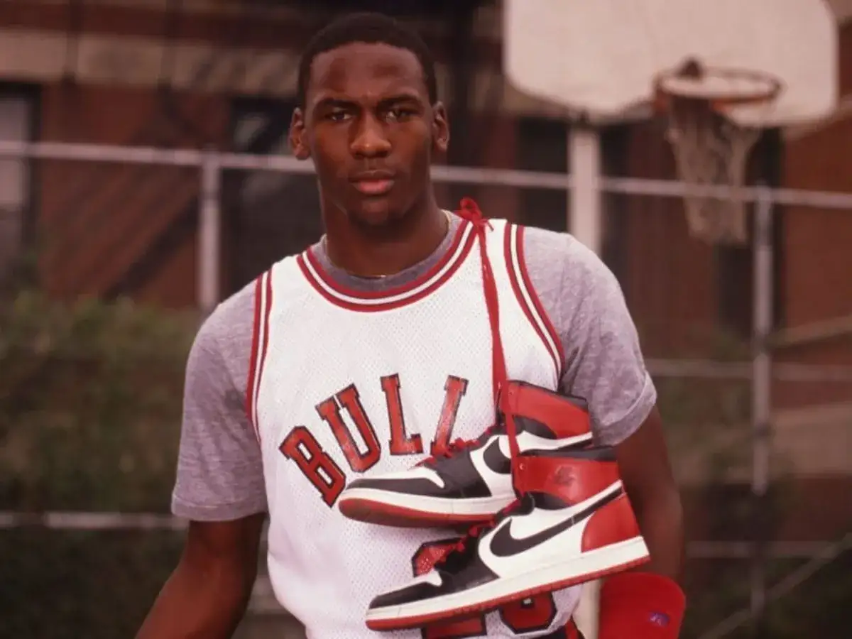 Młody Michael Jordan w koszulce Bulls trzyma buty Air Jordan 1. Czy Jordan to Nike? Tak, to ikona sportu i obuwia.