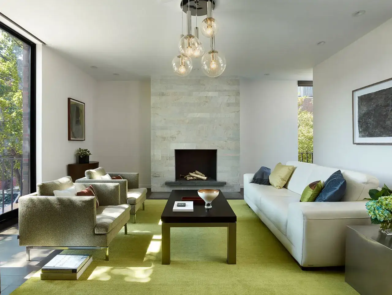 Sof&aacute; blanco y sillones verde y gris combinan en este sal&oacute;n moderno. Chimenea de piedra y alfombra verde vibrante.