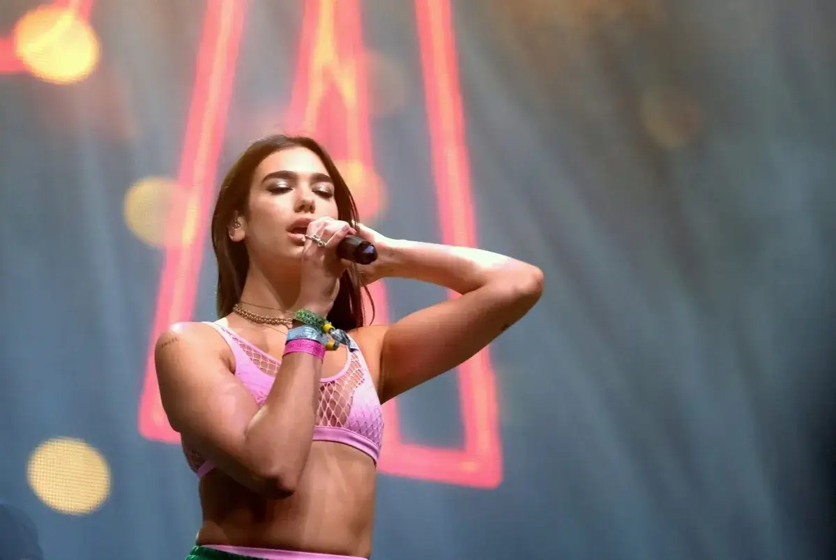 Dua Lipa na jednym z koncertów, śpiewa do mikrofonu w różowym topie.