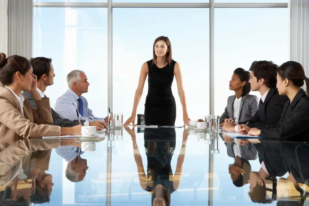 A confident woman stands before a diverse board, embodying the leadership expected in a board chair job description.