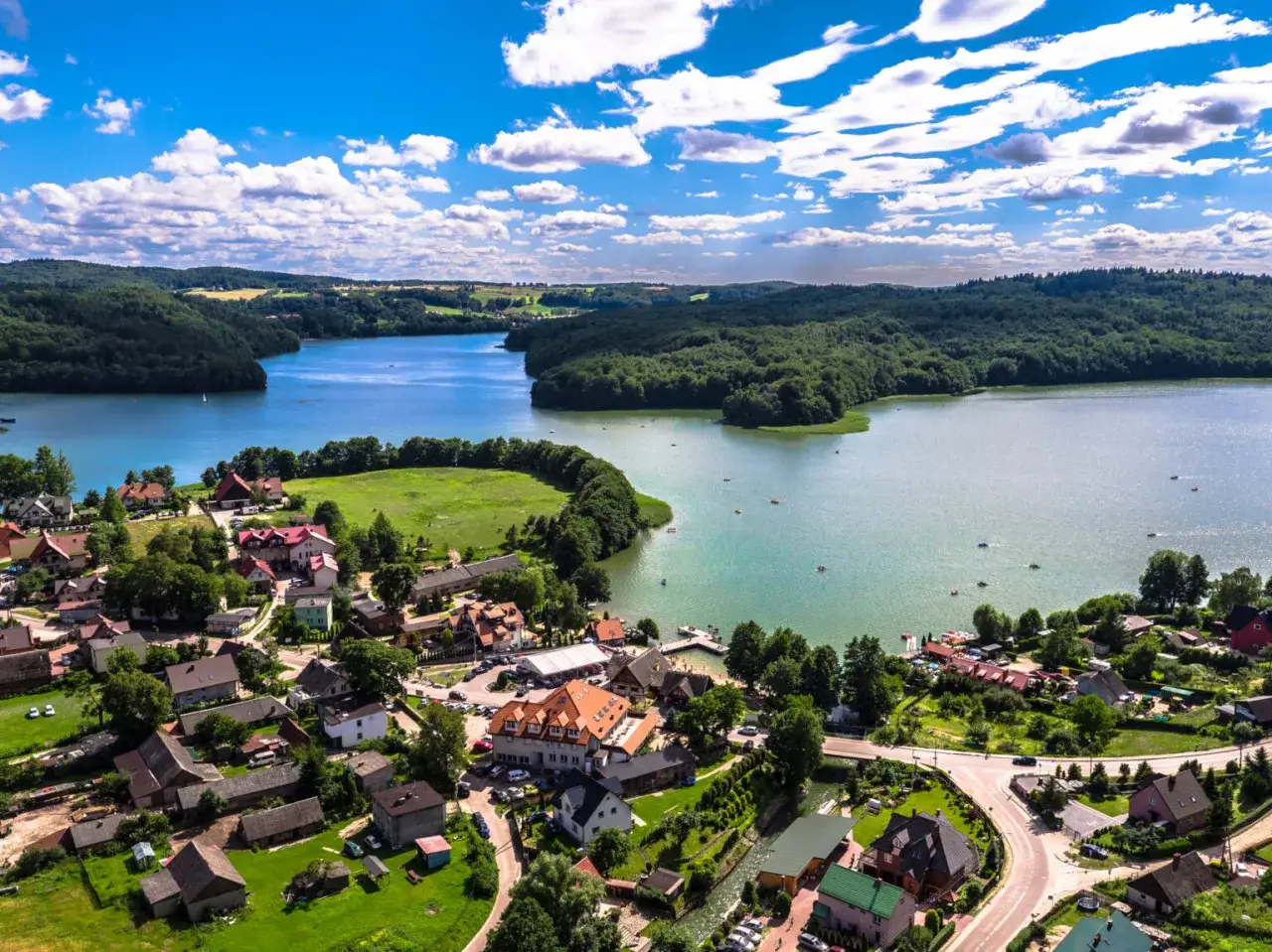 Widok z lotu ptaka na malowniczą wieś Brodnica Górna nad jeziorem, otoczoną lasami.