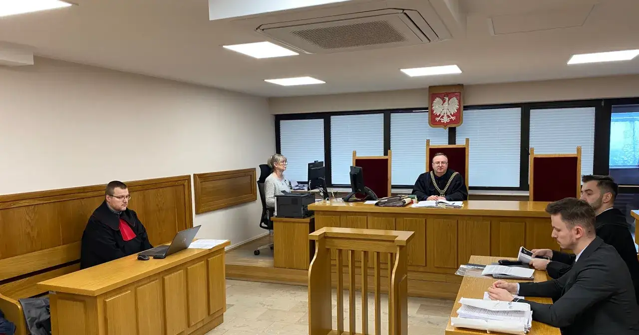Sąd rozpatruje sprawę o zadośćuczynienie. Sędzia w todze z łańcuchem, obok niego ławnicy i adwokaci.