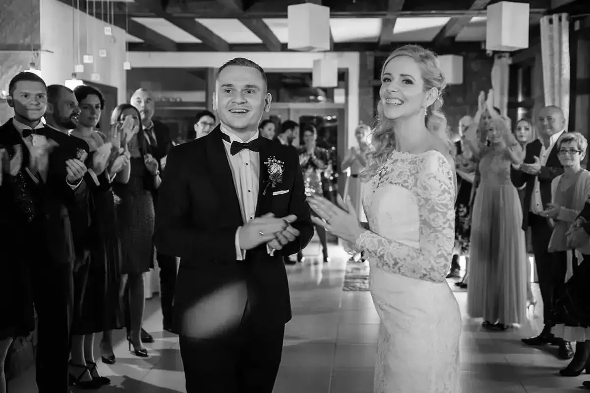 Para młoda wita gości, którzy klaszczą. Zastanawiasz się, ile kosztuje fotograf i kamerzysta na wesele?