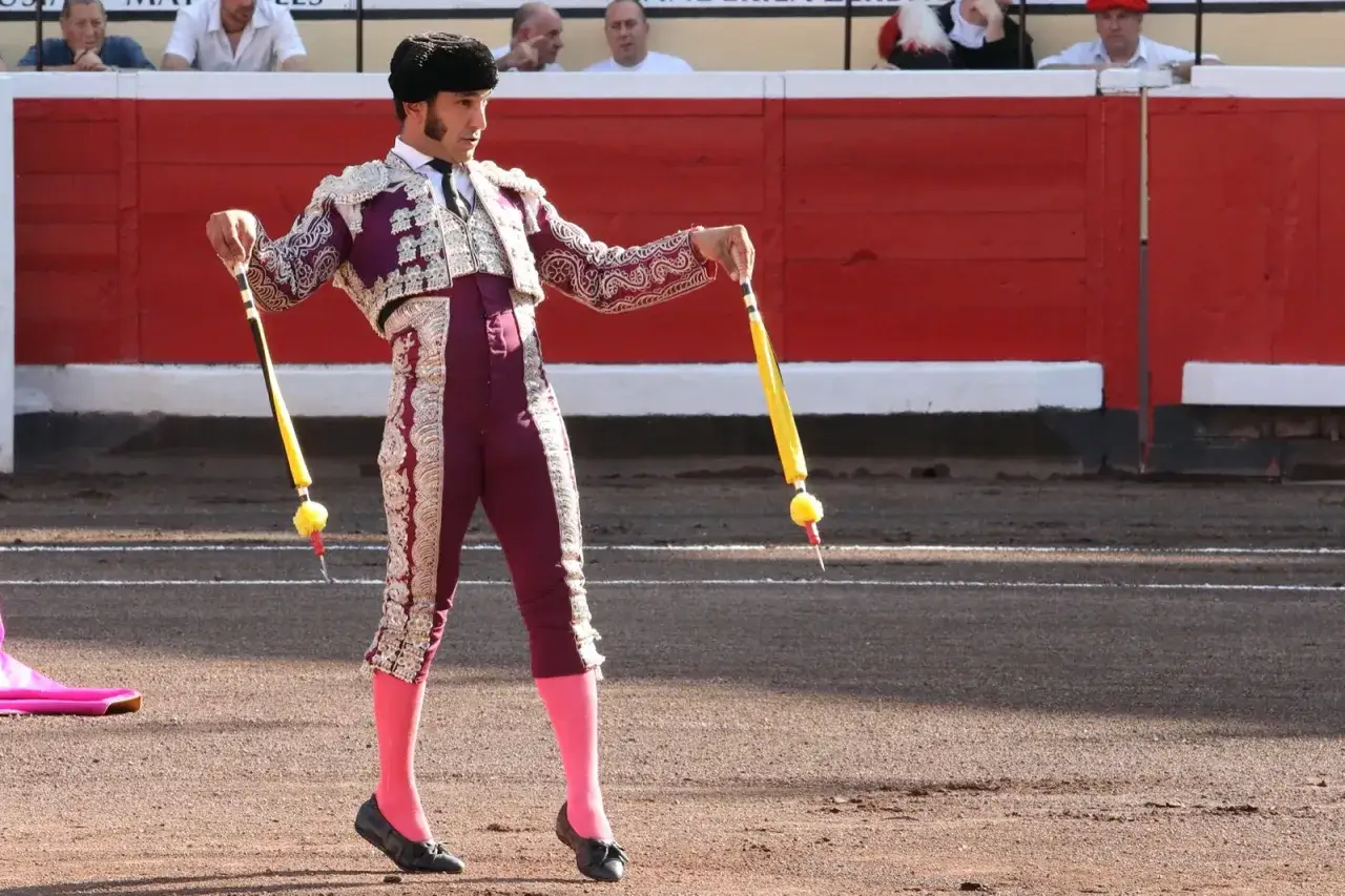 Torero en traje de luces, con banderillas España en mano, listo para la faena.