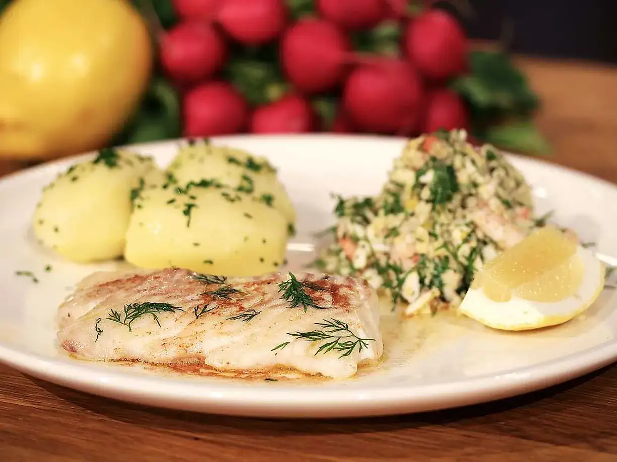 En tallrik med stekt kolja, kokt potatis, en sallad och citronklyfta. Ett perfekt kolja recept för en god middag.