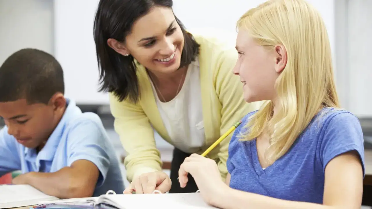 Lehrerin bietet Nachhilfe an. Sie erklärt einer Schülerin etwas, während ein Junge daneben lernt.