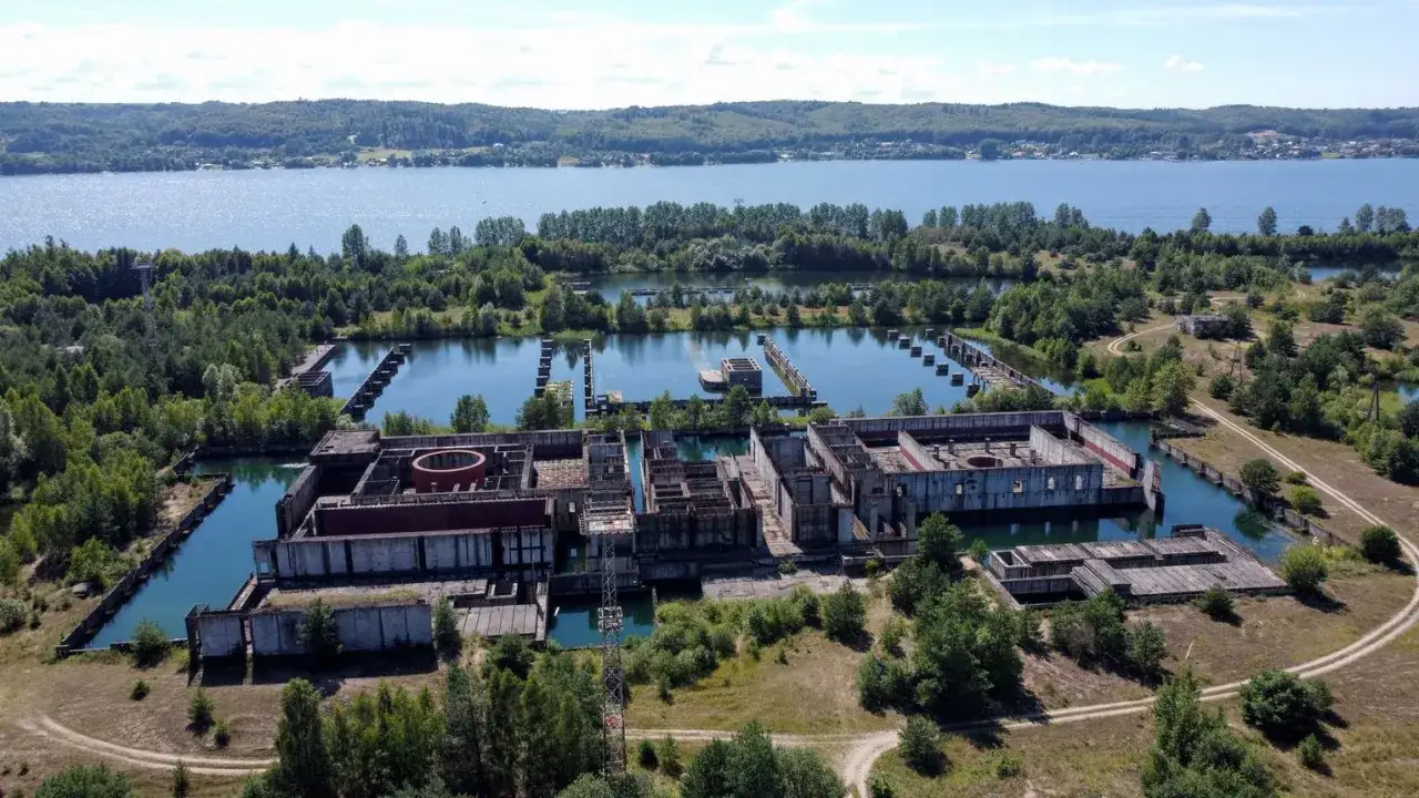 Niedokończona elektrownia atomowa Żarnowiec, otoczona wodą i lasem, z betonowymi konstrukcjami w stanie ruiny.