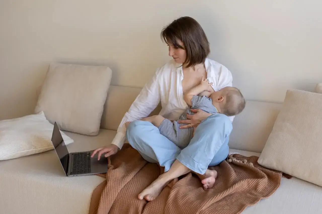 Kobieta karmi piersią dziecko, jednocześnie pracując na laptopie. Warto pamiętać o bezpieczeństwie, np. stosując ibuprofen przy karmieniu piersią.