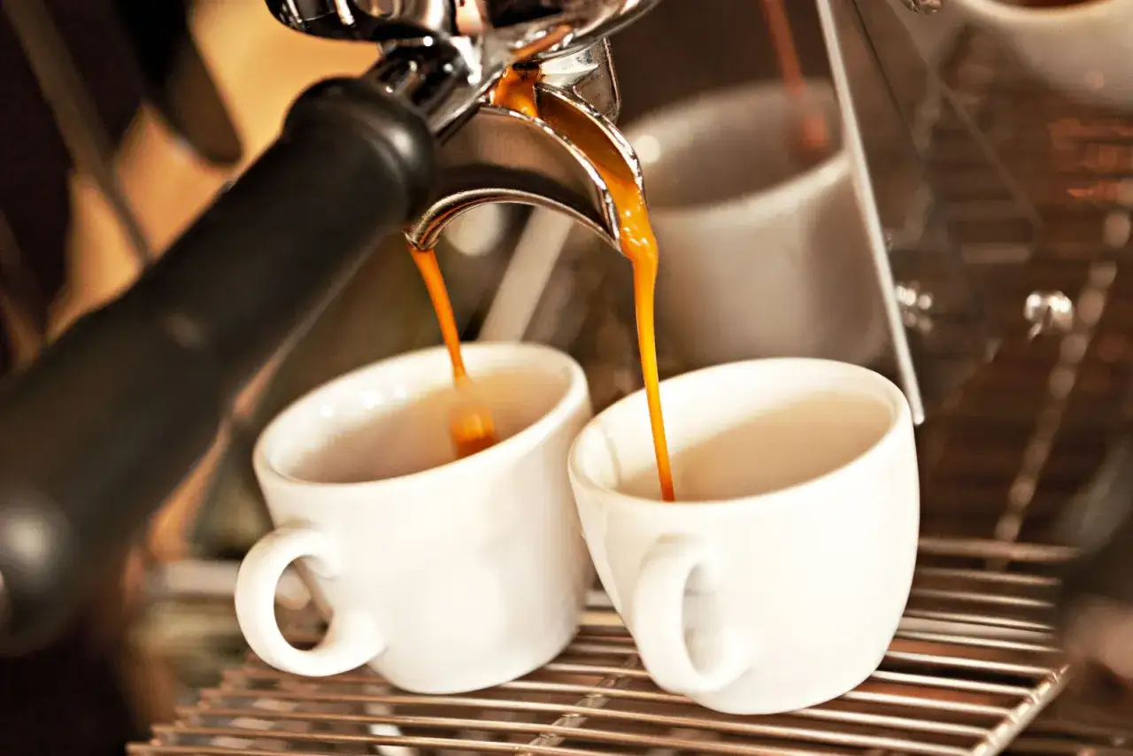 Frisch gebrühter Espresso fließt in zwei weiße Tassen. Die goldbraune Crema de café verspricht puren Genuss.