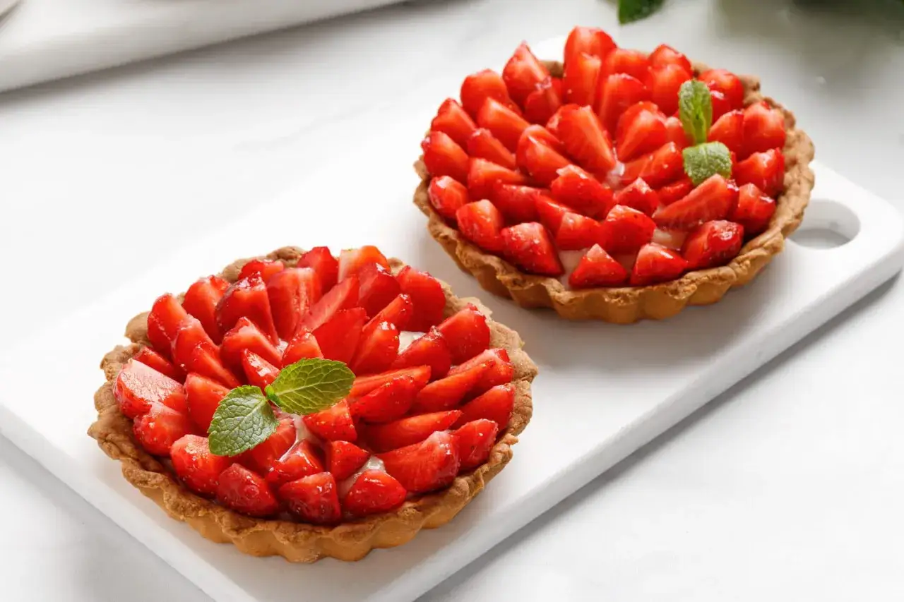 Deux tartelettes aux fraises, garnies de fruits rouges frais et d'une touche de menthe. Un délice qui promet la meilleure tarte aux fraises du monde.