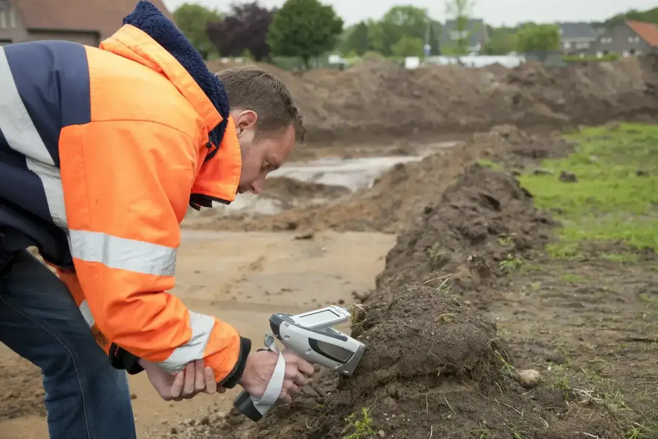 Geolog w pomarańczowej kurtce bada glebę za pomocą urządzenia.