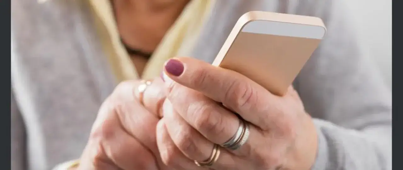 Dłoń z pierścionkami trzyma smartfon. Uważaj na spoofing numeru telefonu, gdy odbierasz nieznane połączenia.