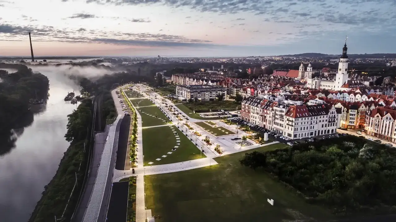 Głog&oacute;w atrakcje: malowniczy widok na miasto o wschodzie słońca, rzekę, park i zabytkową zabudowę.