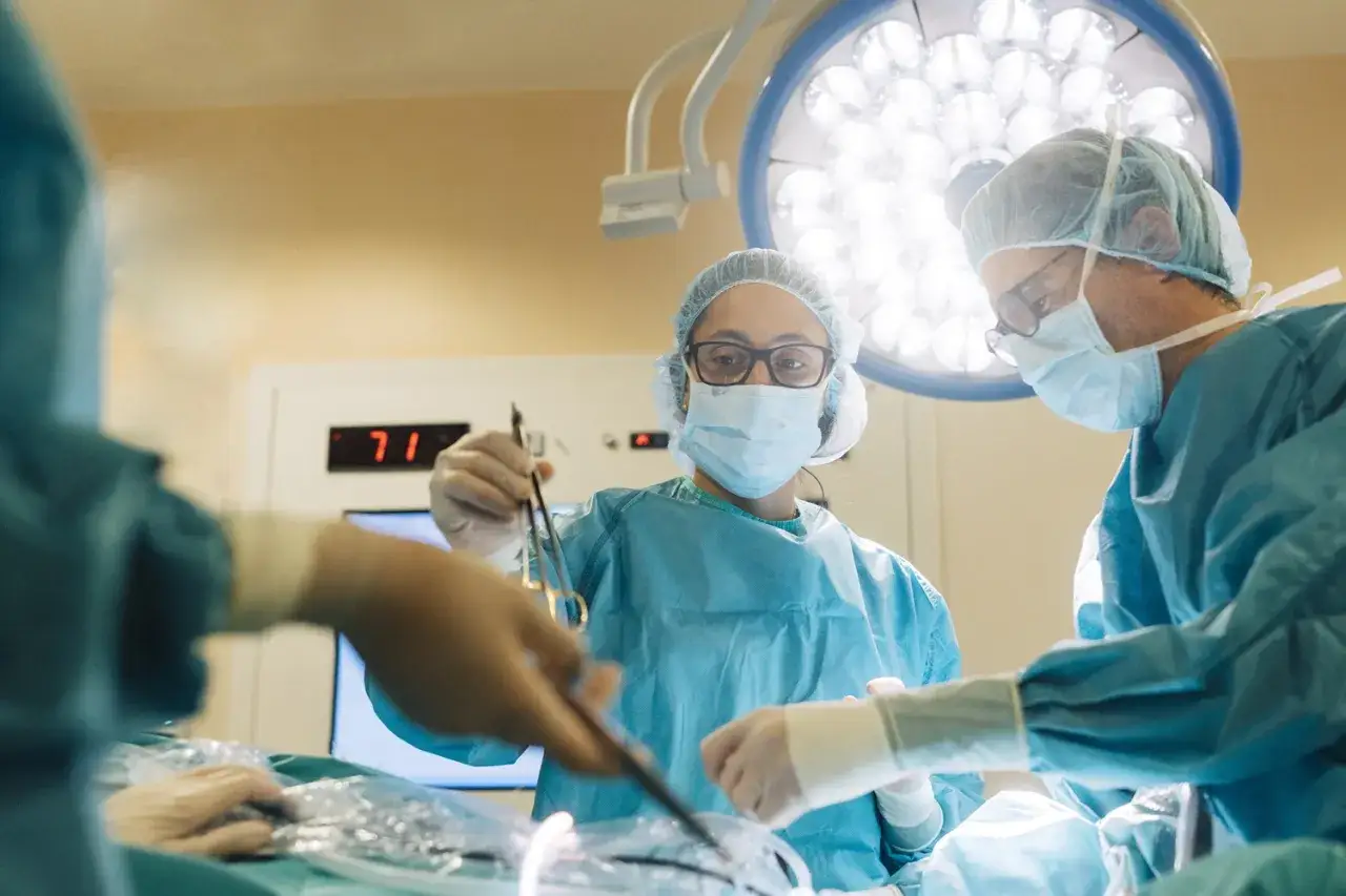 Chirurdzy w maseczkach i fartuchach operacyjnych pracują przy stole operacyjnym pod lampą.