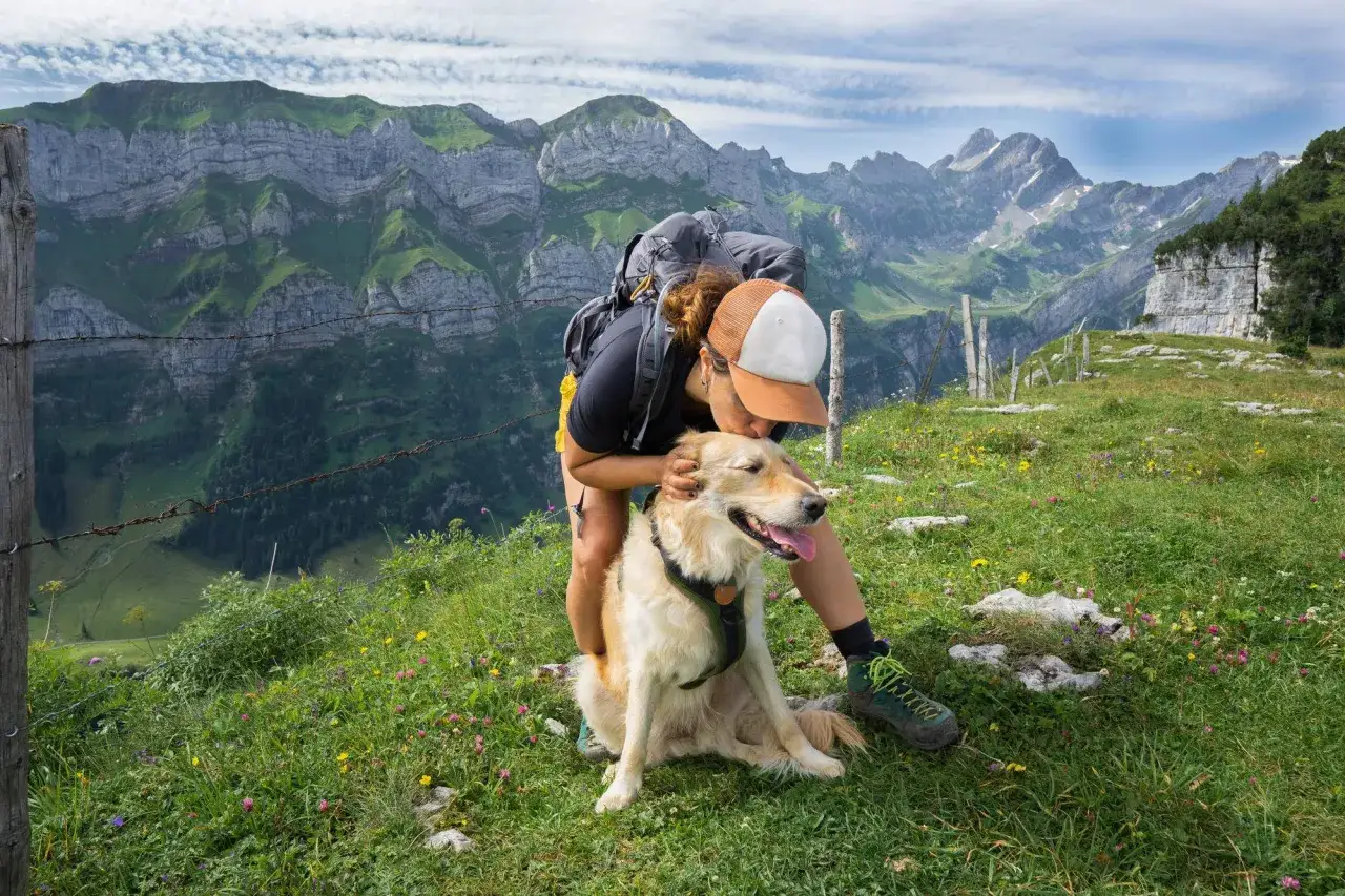 Idealne miejsce, gdzie na wakacje z psem: kobieta z plecakiem całuje swojego golden retrievera na tle majestatycznych g&oacute;r.