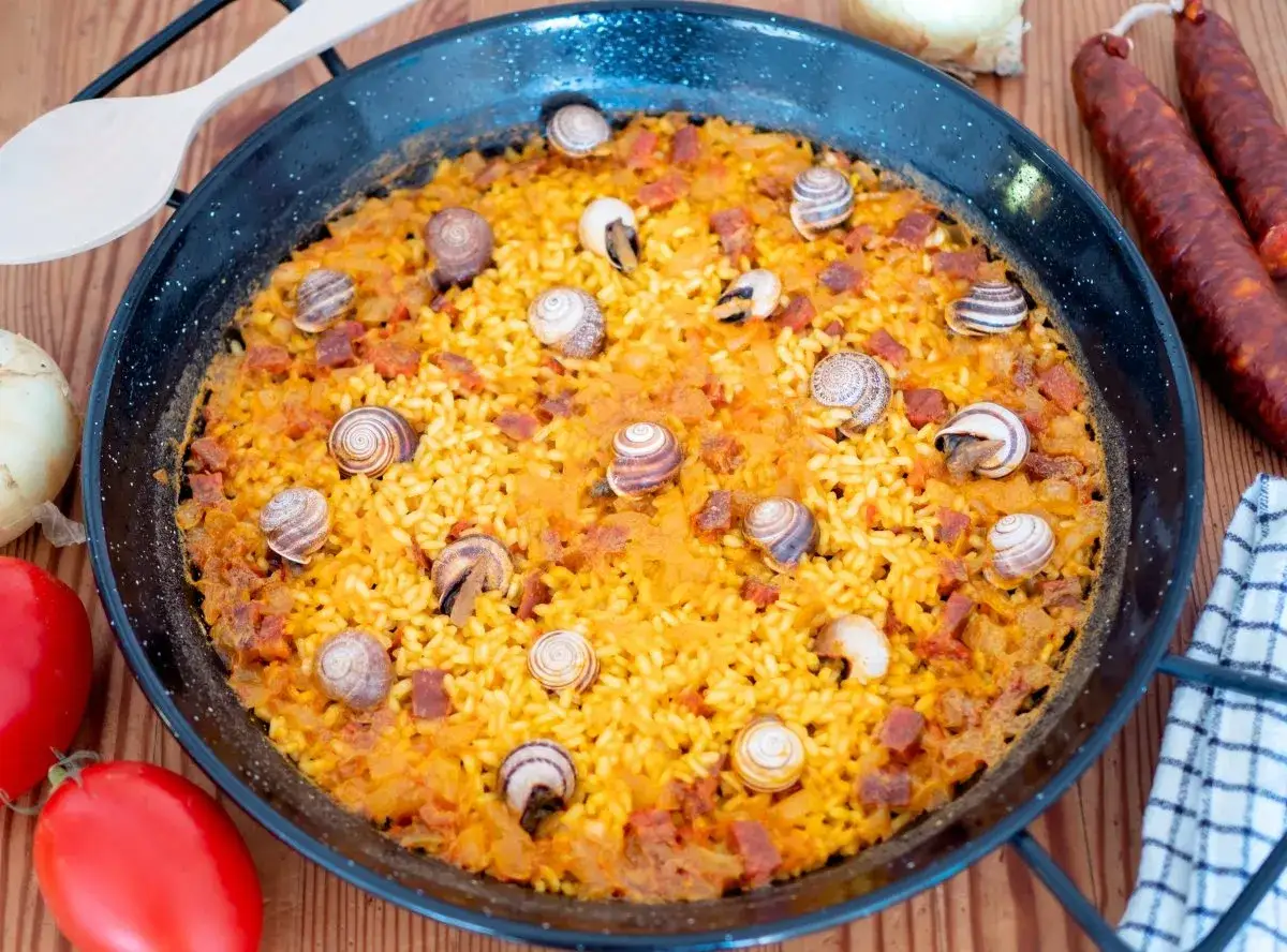 Arroz con caracoles, un plato tradicional español con arroz amarillo, trozos de chorizo y caracoles cocidos, servido en una paellera.