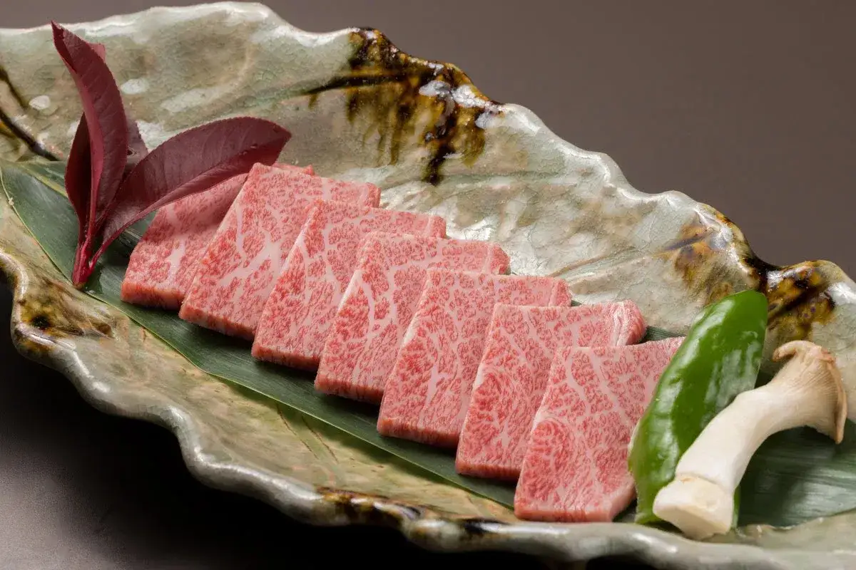 Kawałki soczystej krowy wagyu z marmurkowym tłuszczem, ułożone na liściu, z dodatkiem papryki i grzyba.