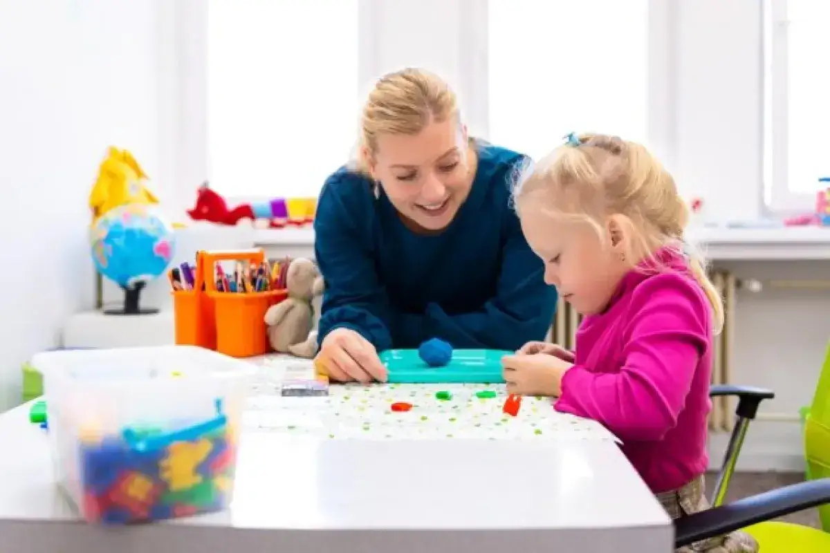 Terapia logopedyczna z dzieckiem z zaburzeniami si a mowa. Terapeuta i dziecko lepią z plasteliny.