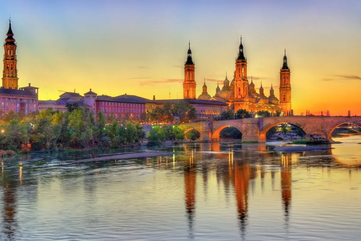Zachód słońca nad rzeką Ebro w Saragossie. Bazylika del Pilar i kamienny most odbijają się w wodzie.