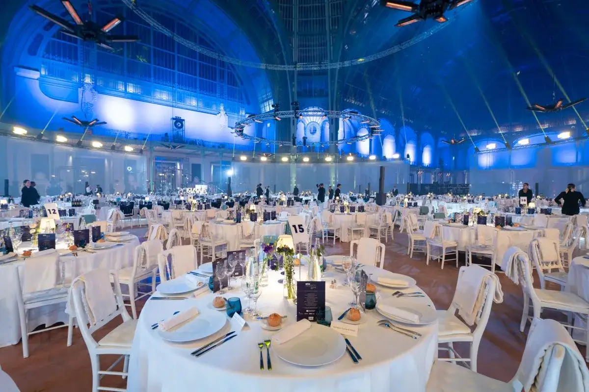 Salle de réception élégante, tables dressées pour un dîner de gala. L'ambiance bleue suggère une soirée où l'on pourrait rencontrer un homme riche.