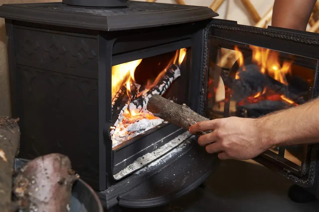 Mano añade leña a una chimenea encendida. La pregunta es: ¿cuál es la mejor leña para chimenea?