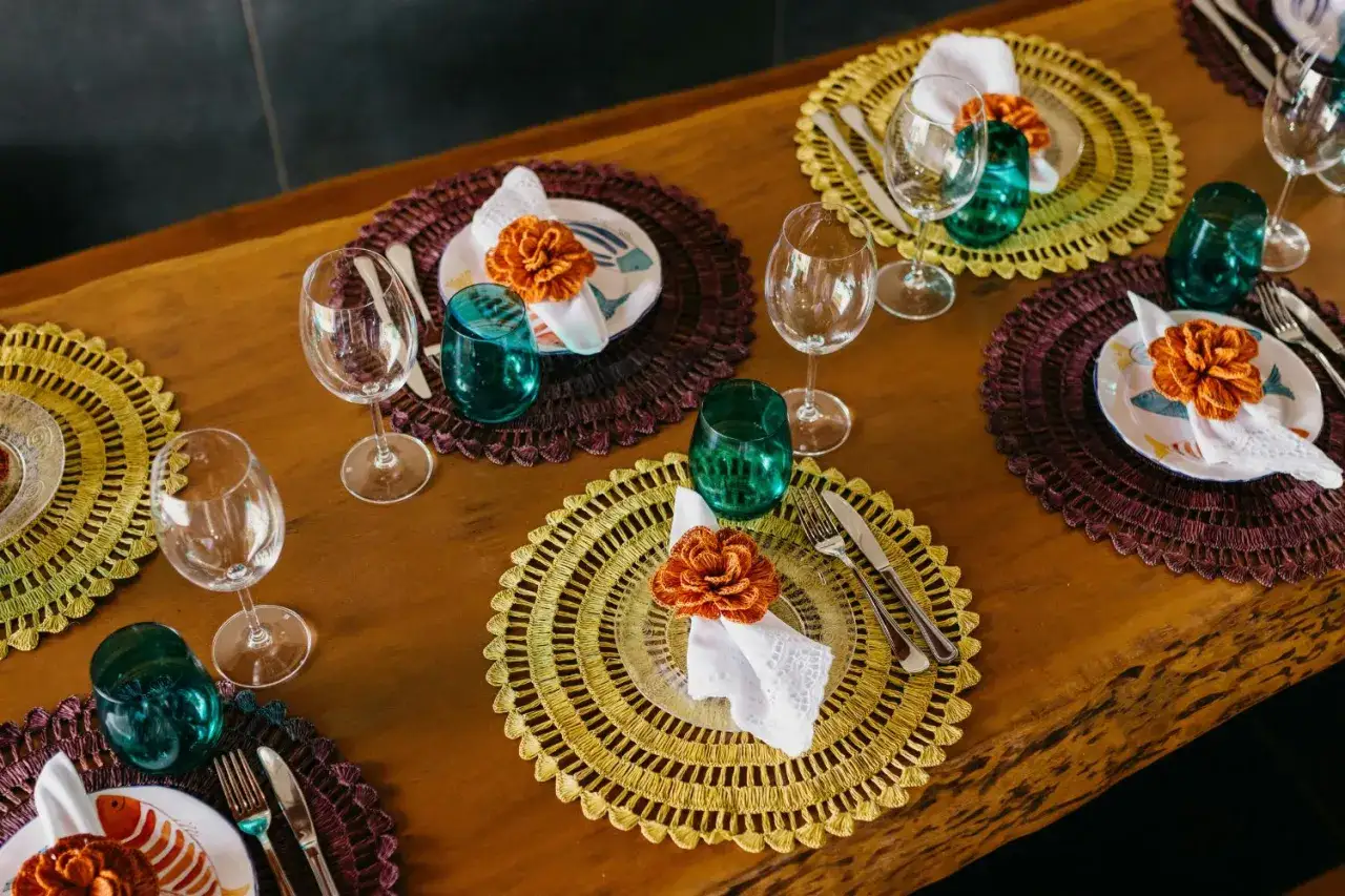 Sottopiatti eleganti fai da te in rafia, con decorazioni floreali arancioni e bicchieri verdi, creano un'atmosfera vivace per la tavola.