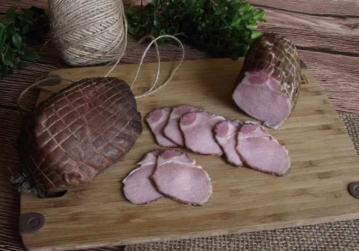 Wędzenie schabu na desce. Całe i pokrojone plastry wędzonego mięsa, sznurek i zieleń w tle.