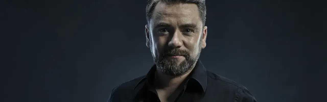 Kuba Badach w czarnej koszuli, z zarostem, patrzy wprost przed siebie. Widać, że wracam do siebie po trudach.