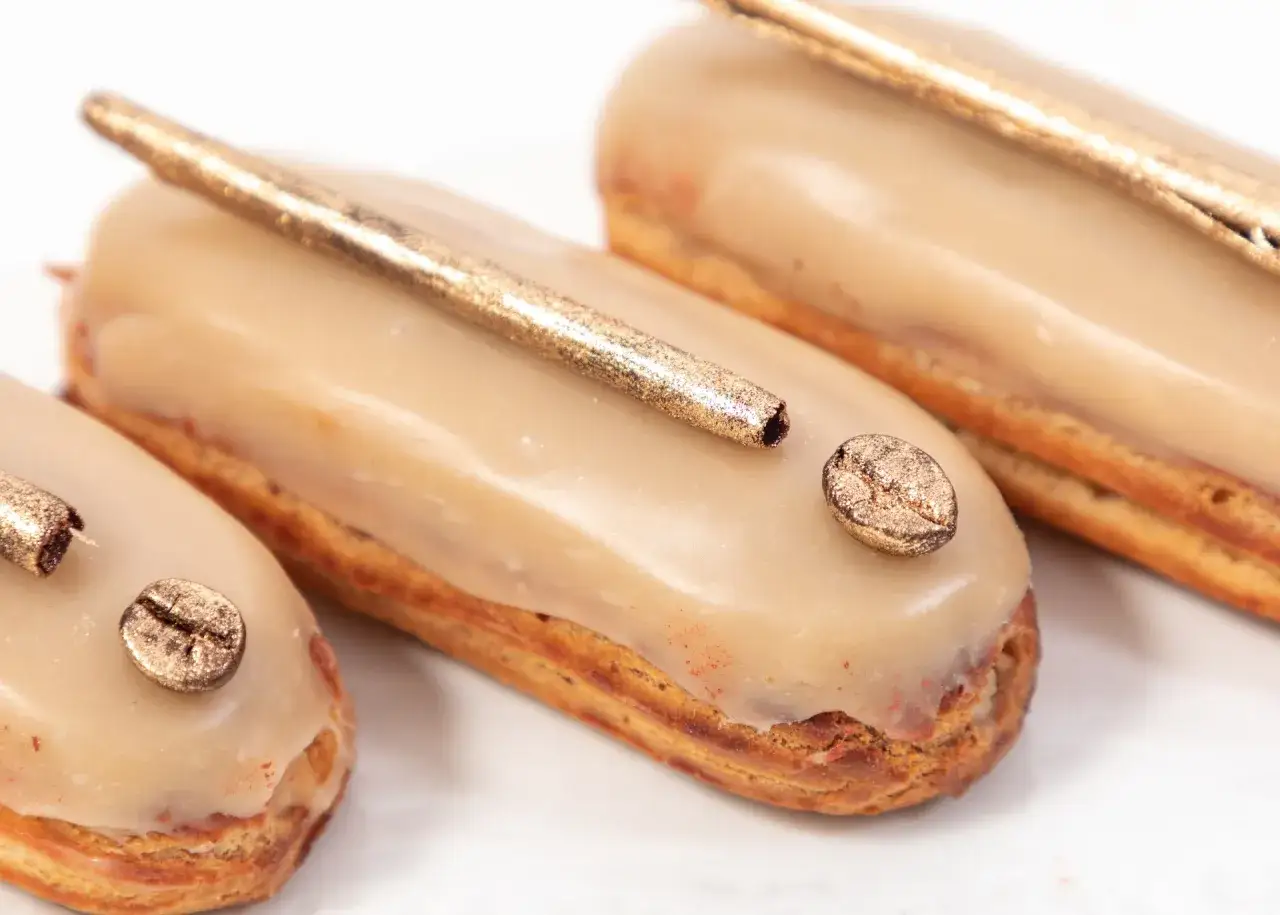 Trois éclairs gourmands, glacés d'une crème pâtissière café onctueuse, ornés d'une touche dorée et d'un grain de café scintillant.