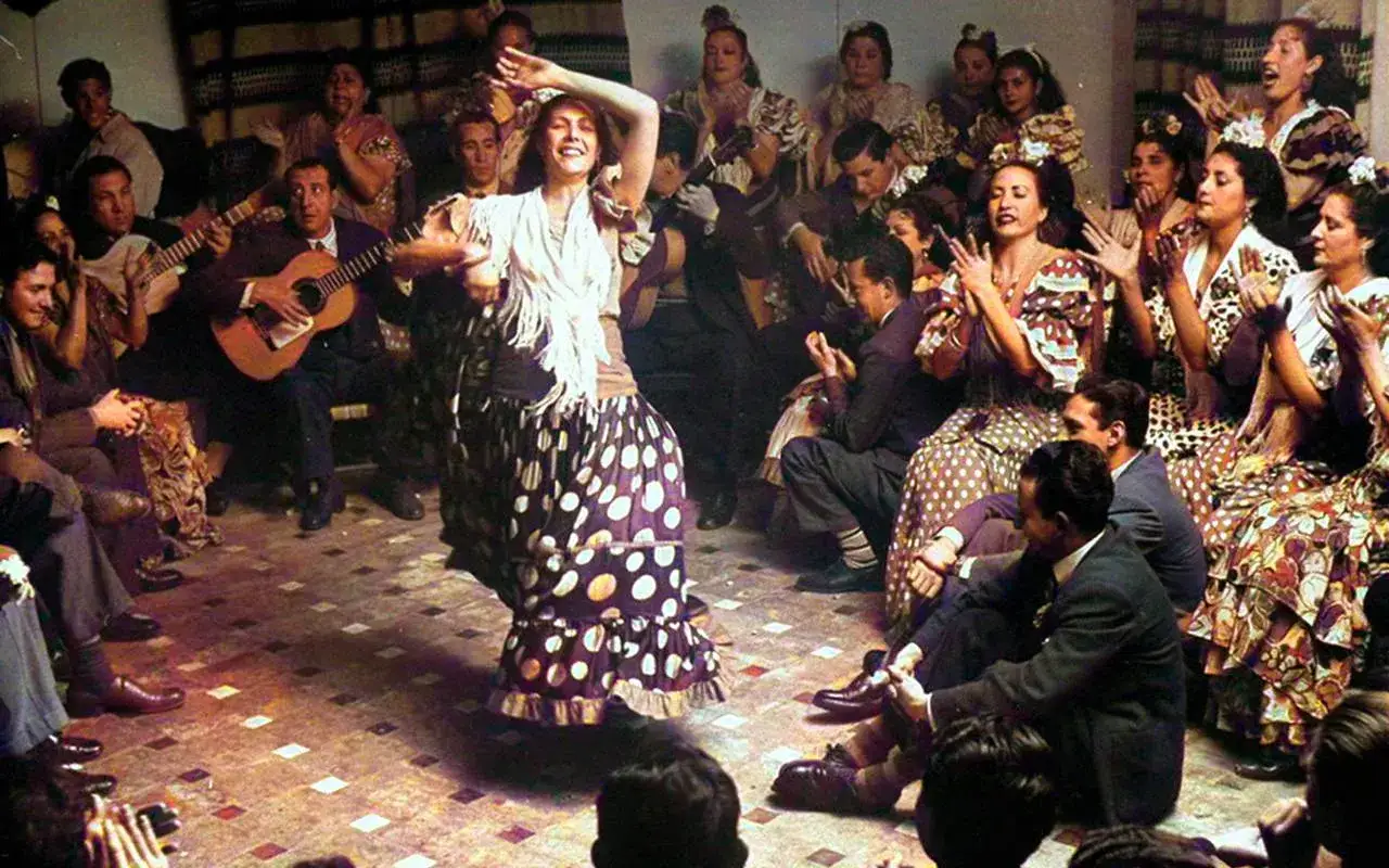 Una bailaora flamenca, con su falda de lunares, cautiva a un p&uacute;blico que aplaude. El guitarrista acompa&ntilde;a la escena, evocando el zambra significado.