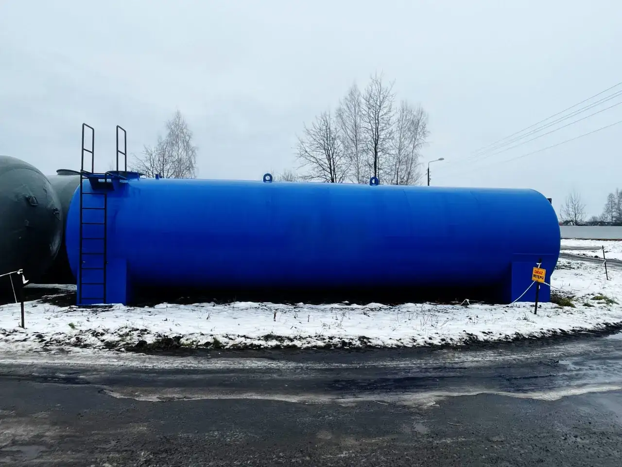 Duży, niebieski zbiornik przemysłowy, stojący na ośnieżonym terenie. Obok widać szary zbiornik. To widok z zachodniej części globalnej infrastruktury.
