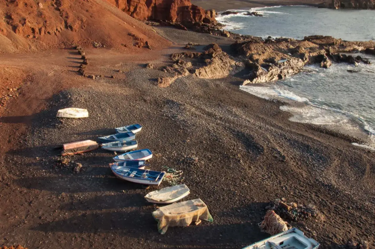 Łodzie na czarnej plaży, skaliste wybrzeże i łagodne fale. Idealna pogoda na Lanzarote.