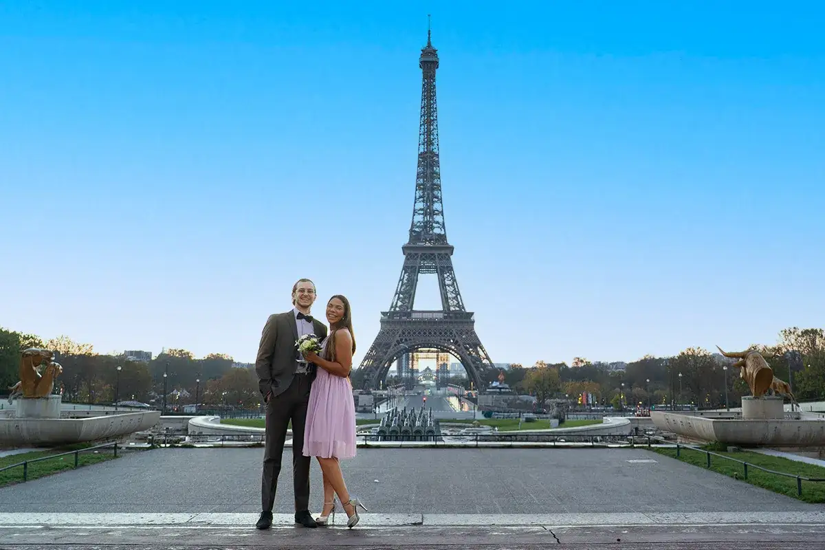 Un couple heureux pose devant la Tour Eiffel, la jeune femme tenant un bouquet.