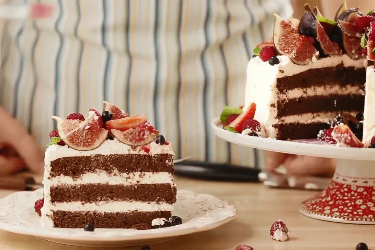 Obłędny tort czekoladowy z mascarpone i owocami: kawałek na talerzyku i cały tort na paterze, ozdobione figami, malinami i borówkami.