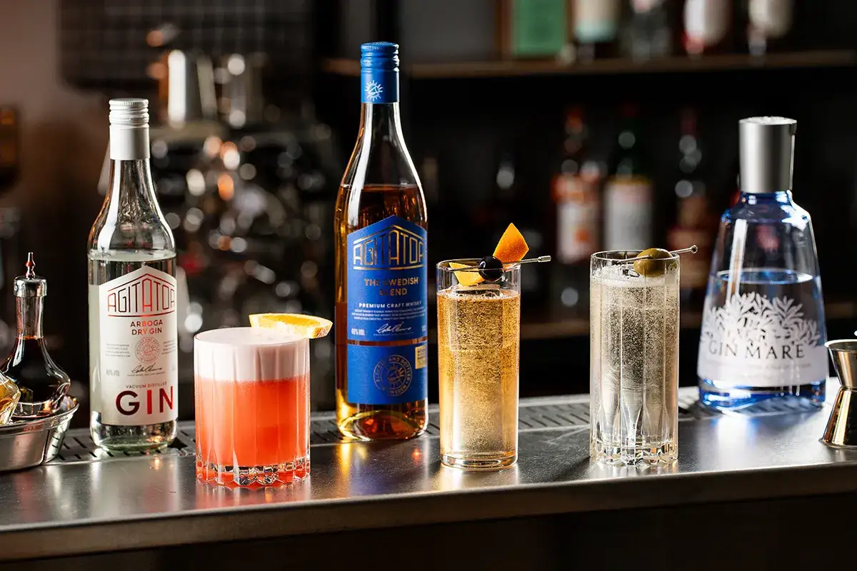 Flera svenska drinkar med gin, whisky och andra ingredienser st&aring;r uppradade p&aring; en bardisk.