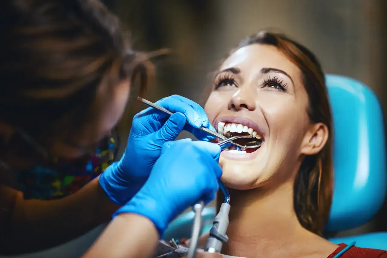 Dentystka w niebieskich rękawiczkach zakłada aparat na zęby uśmiechniętej pacjentki.