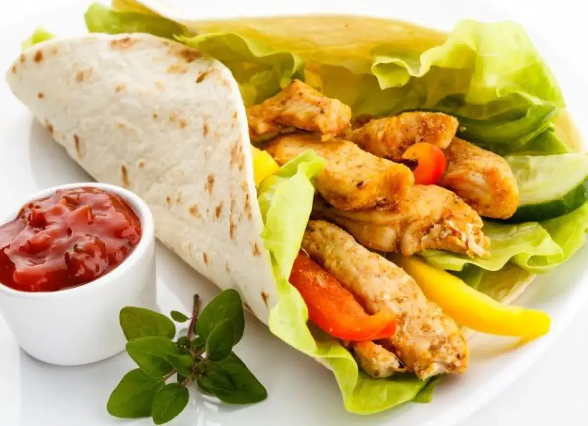 Pyszny kebab w picie z soczystym kurczakiem, chrupiącą sałatą, kolorową papryką i orzeźwiającym ogórkiem, podany z sosem pomidorowym.