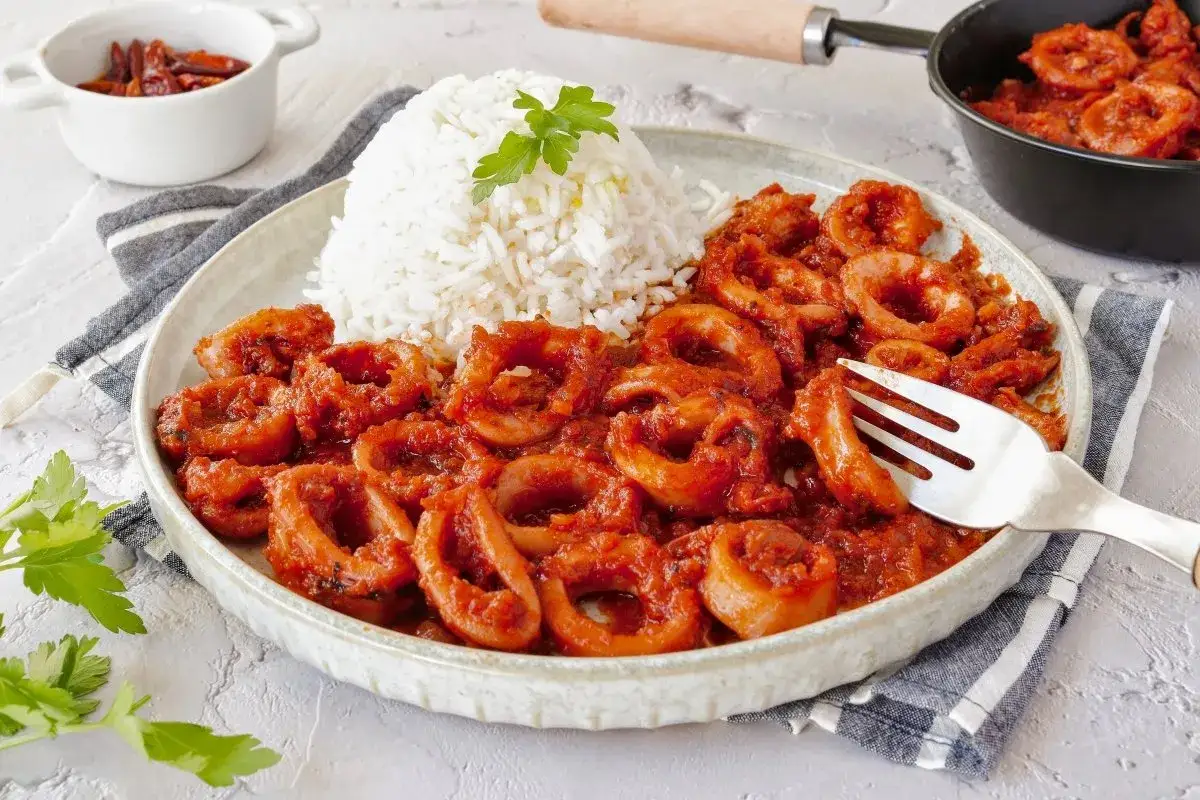 Calamares en salsa roja, servidos con arroz blanco y decorados con perejil. Un plato apetitoso listo para disfrutar.