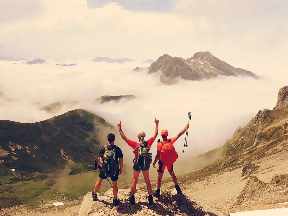 Tres excursionistas celebran en la cima de los Picos de Europa, con un mar de nubes a sus pies y picos majestuosos emergiendo.