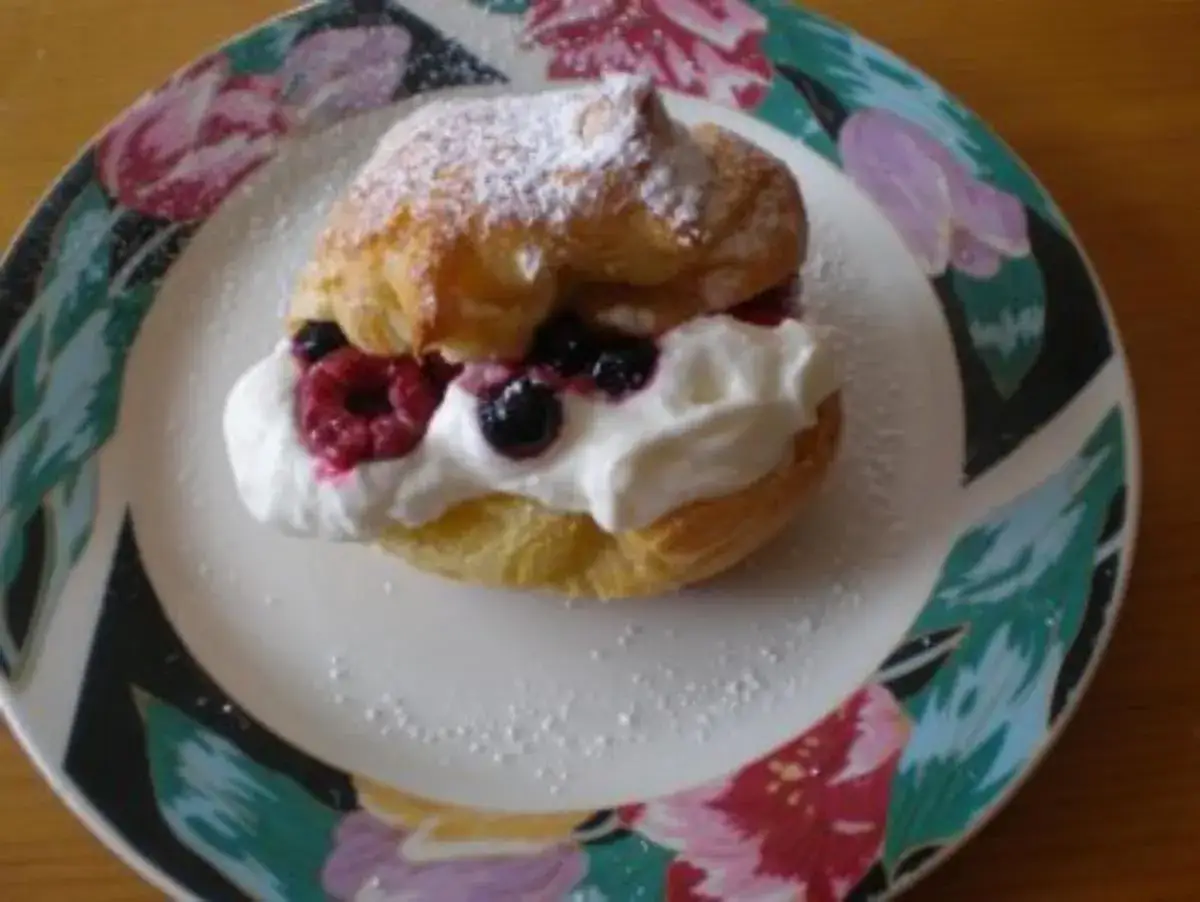 Ein köstlicher Windbeutel gefüllt mit Sahne und frischen Beeren, bestäubt mit Puderzucker. Ein süßer Genuss!